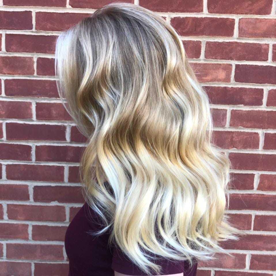 Woman with long, wavy blonde hair stands against a brick wall.